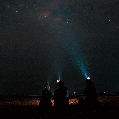 Three people wearing head torches pointing up to the night sky and milkyway